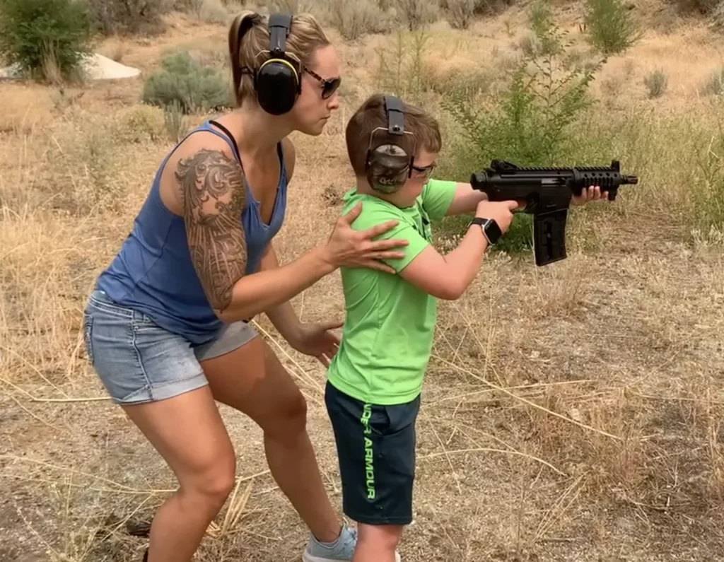 guiding young kids in gun safety outdoors, both wearing hearing protection and safety glasses.
