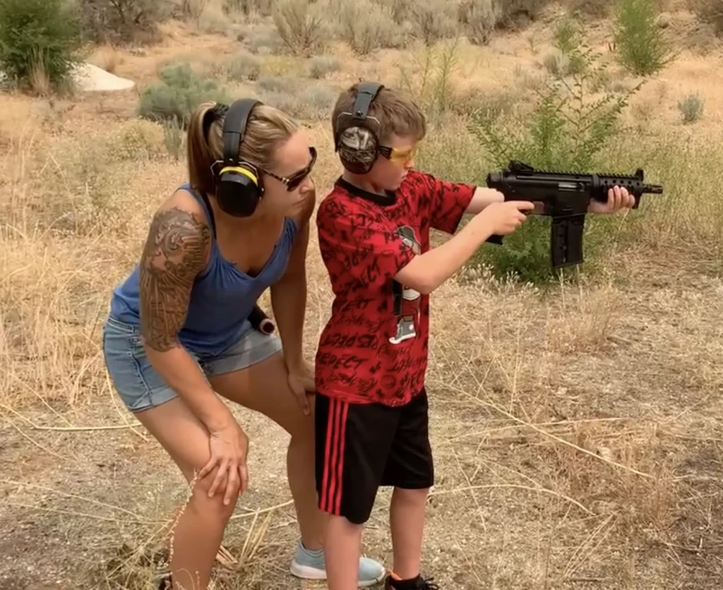 Mom teaching son gun safety outdoors, both wearing ear protection and safety glasses.